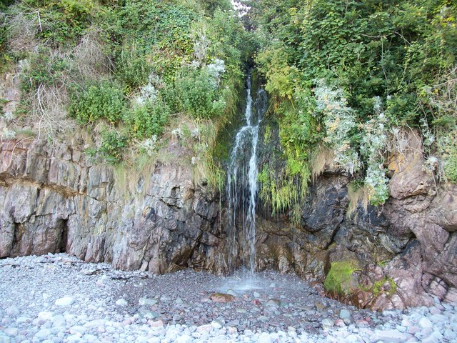 A small waterfall cascades off the rock edge, making a pool in the pebbles below at Glenthorne beach