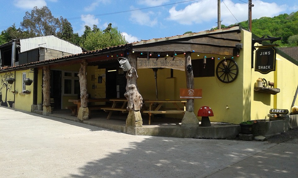 A yellow building with benches outside and a sign for Jim's shack at Bere Cider Company