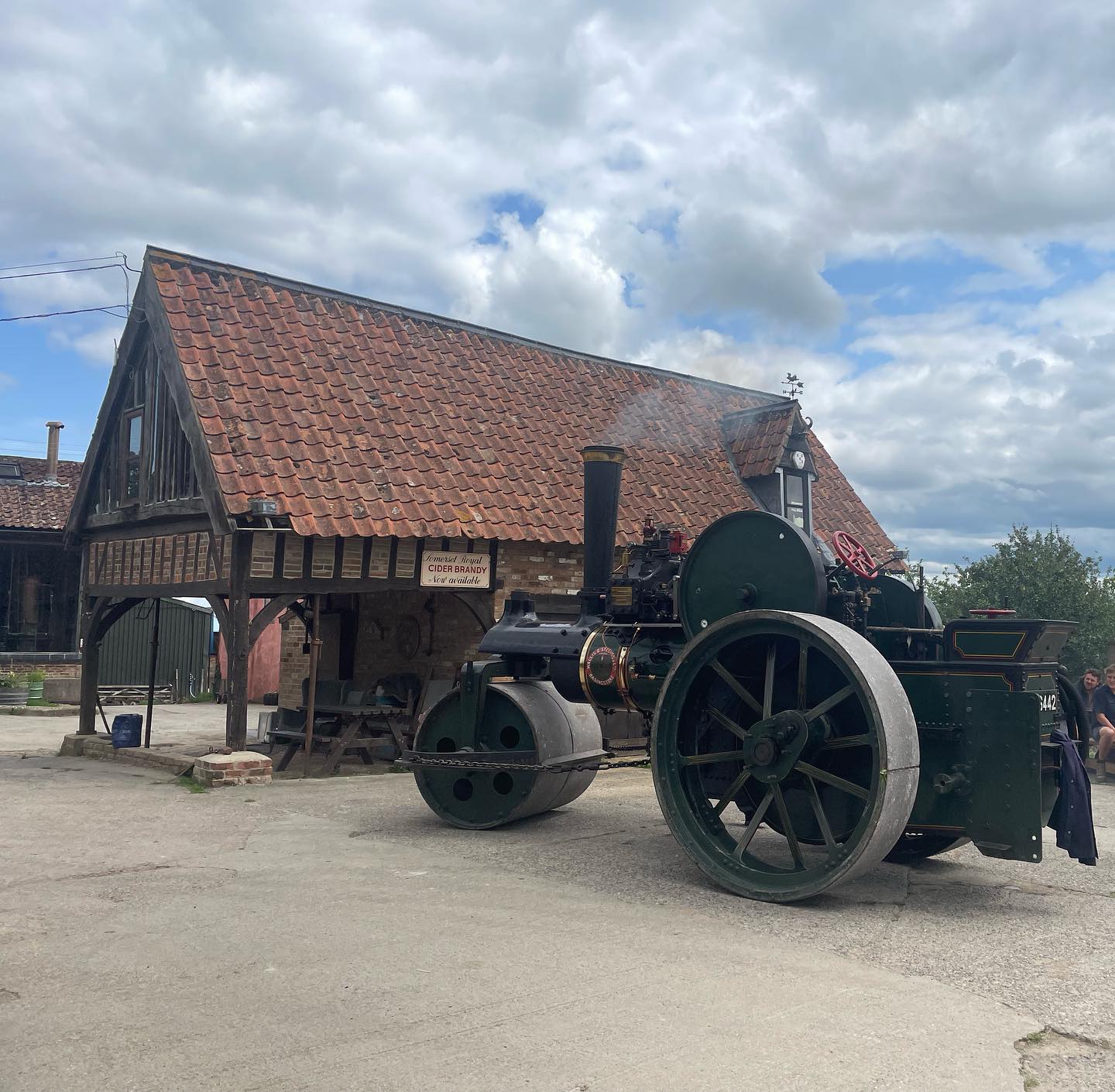 A green steam roller sits in a concrete yard in front of an old barn with tiled roof | The Somerset Cider Brandy Company & Burrow Hill Cider